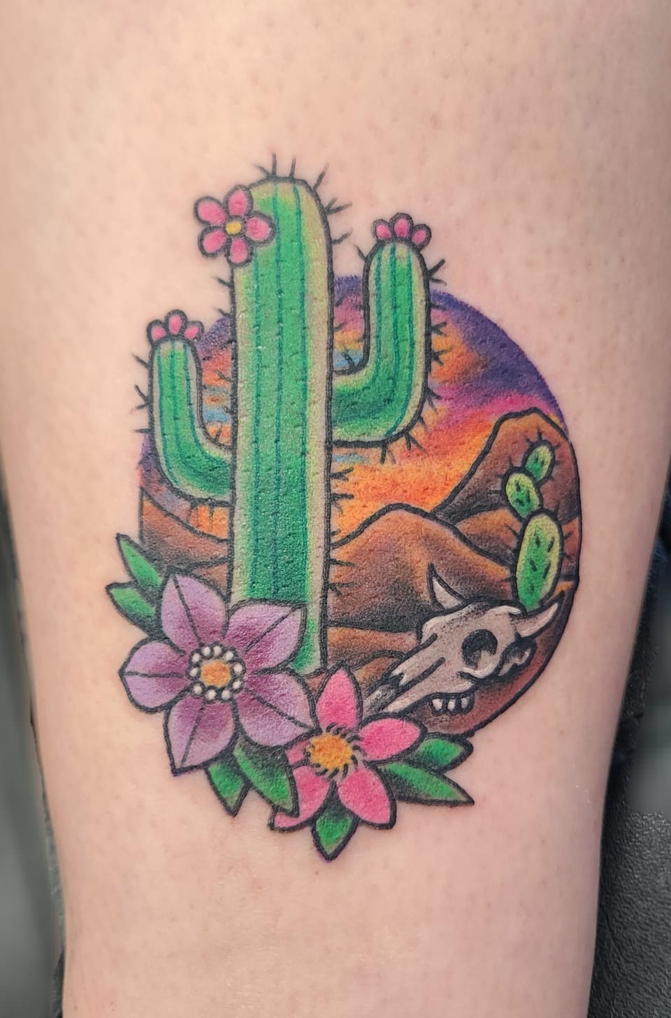 A cactus, flowers, desert hills and an animal skull form a colorful tattoo.