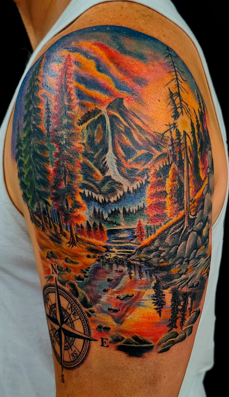 A bright forest and mountain landscape tattoo wraps an upper arm.