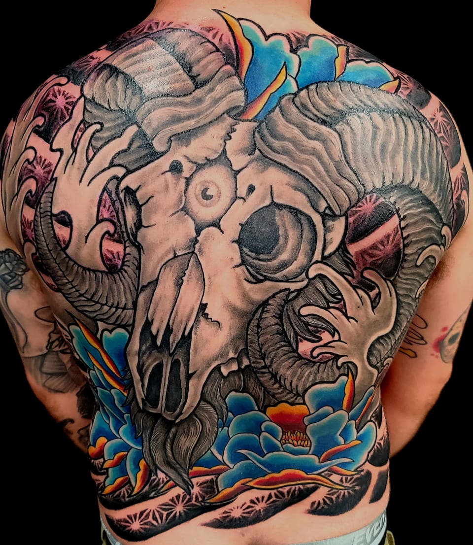 A horned animal skull and blue flowers cover an upper-arm tattoo.