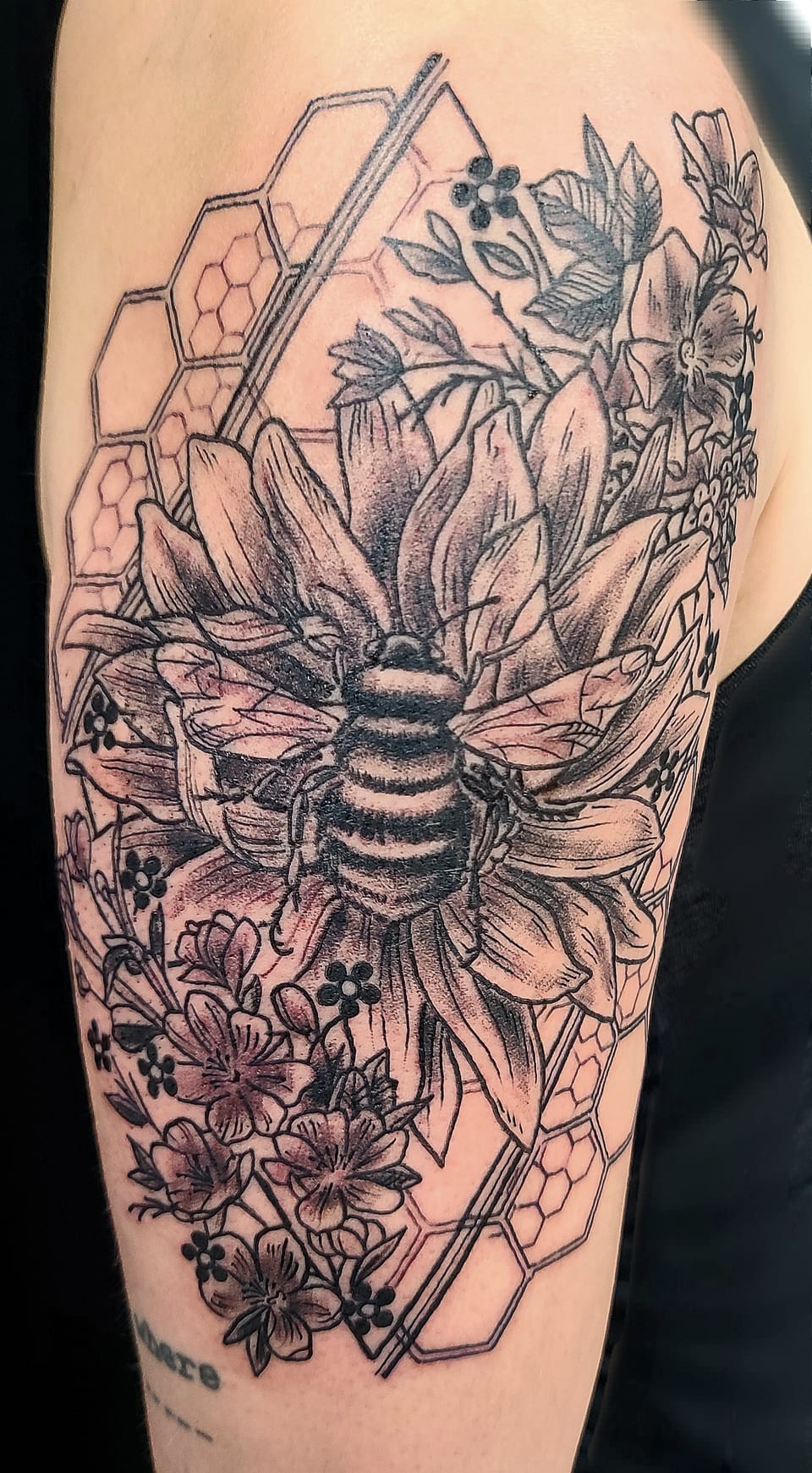 A bee and botanical linework sit inside a geometric hand tattoo.