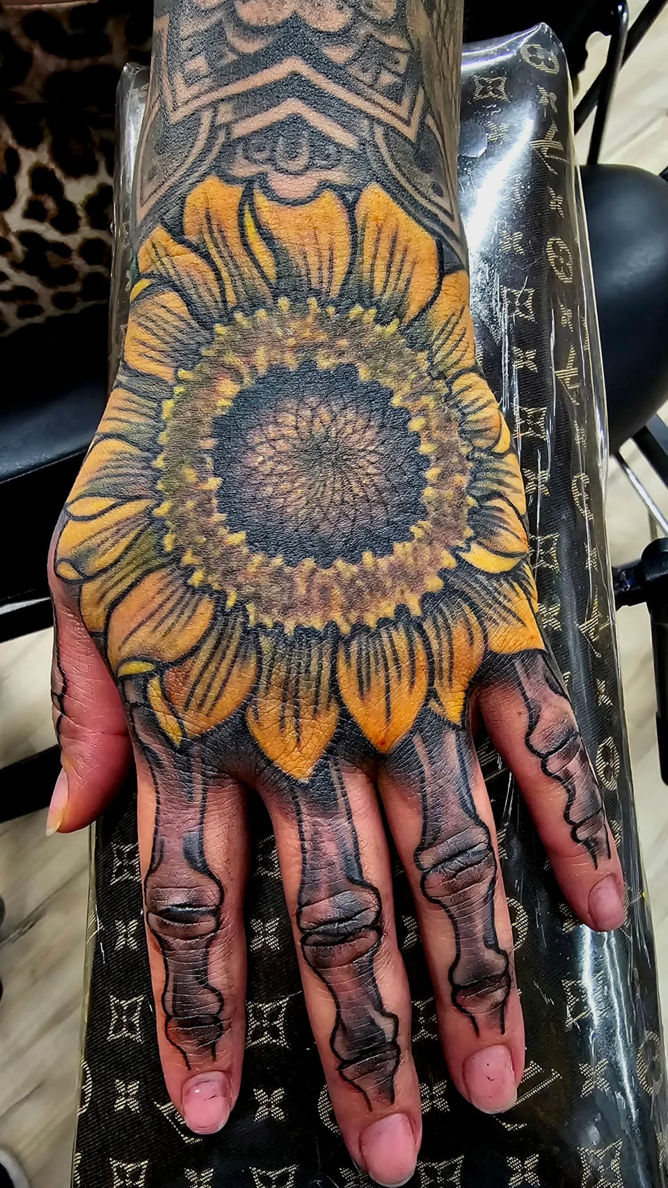 A yellow sunflower tattoo covers the back of a hand.