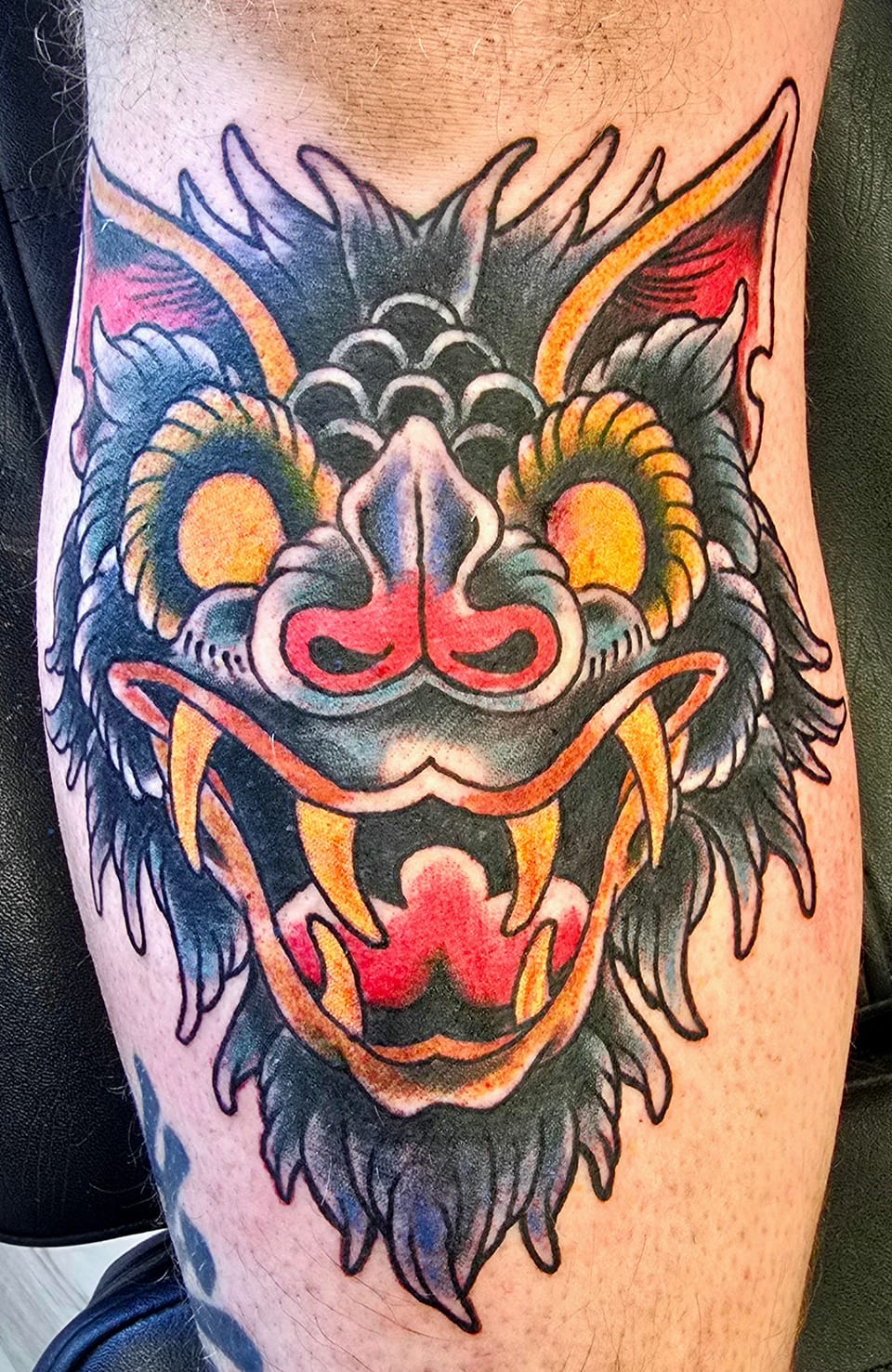 A blue, gold and red guardian face fills a colorful leg tattoo.