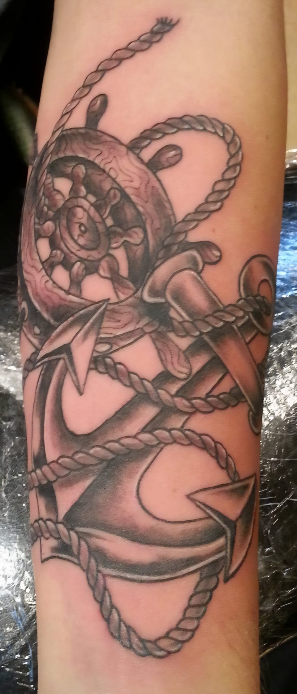 A black and grey cartoon sailor holds a ship wheel in an arm tattoo.