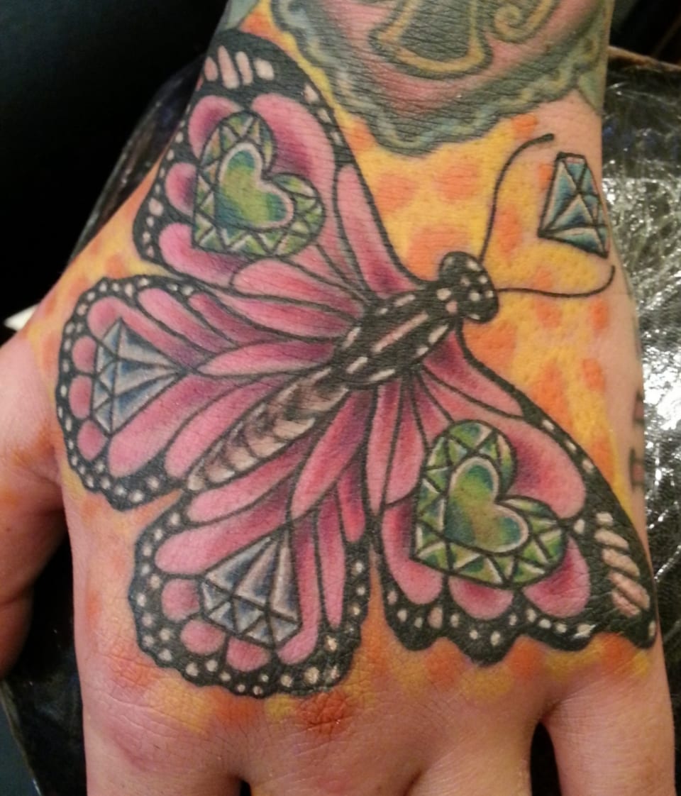 A pink and green butterfly tattoo spreads across a hand.
