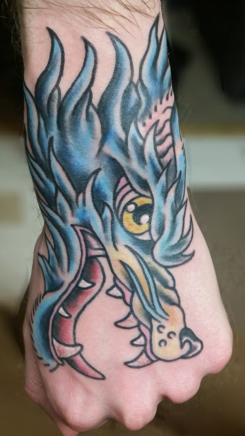 A blue dragon tattoo curves across the hand and wrist.