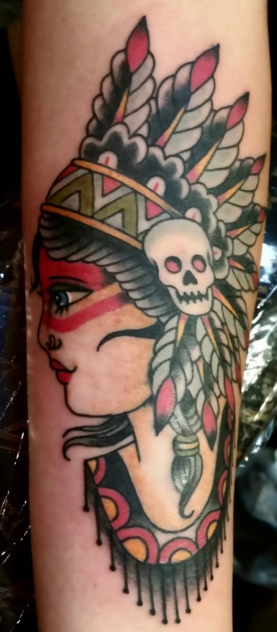 A woman in a feathered headdress fills a colorful leg tattoo.