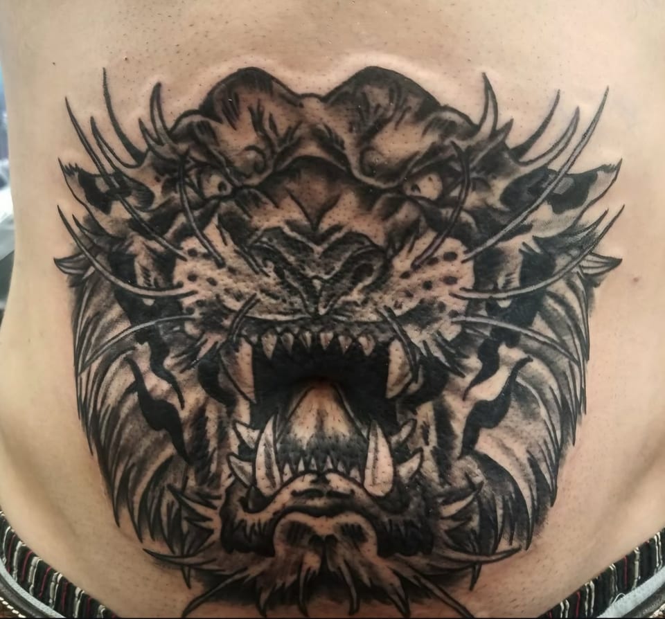 A black and grey roaring tiger face tattoo fills the abdomen.