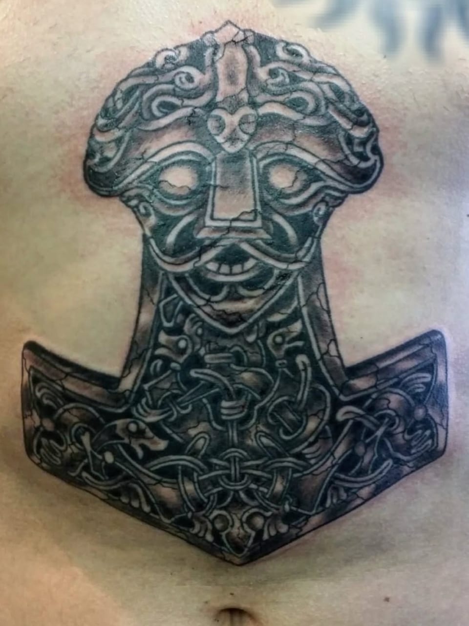An ornamental hammer tattoo has a face and curling black patterns.