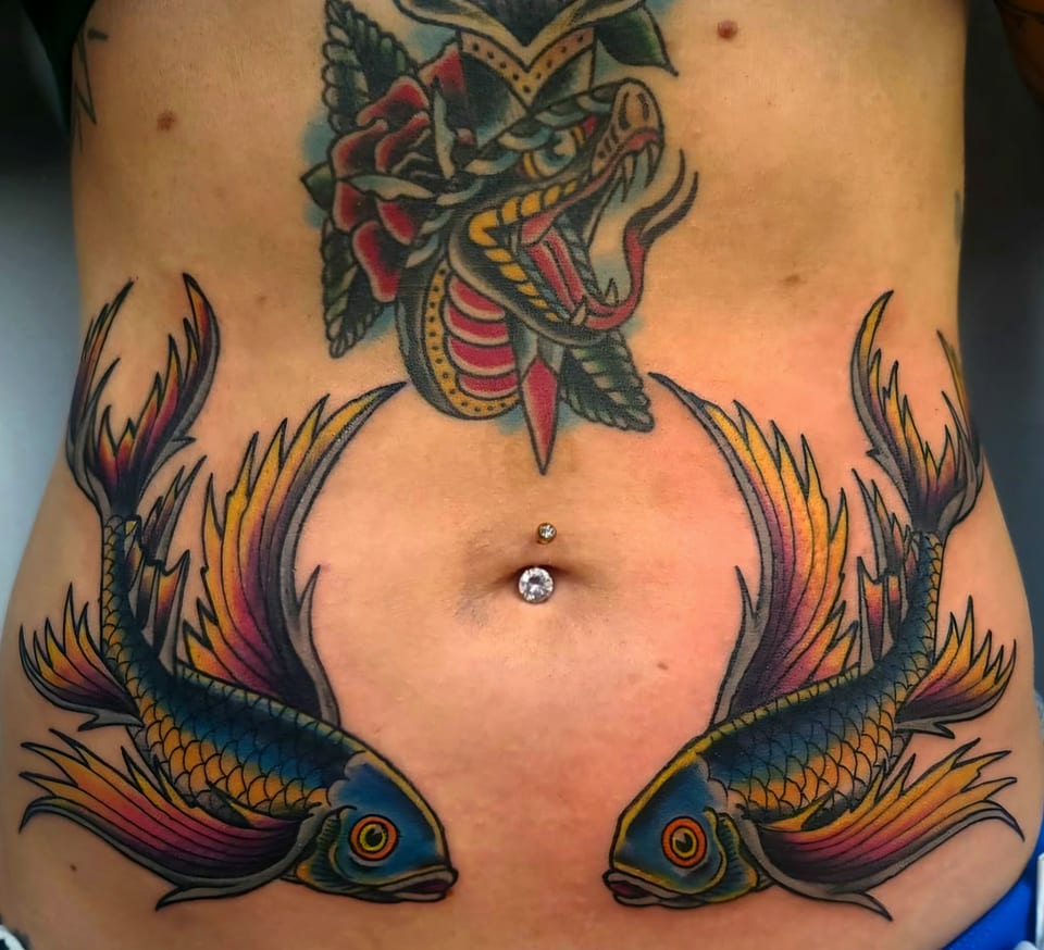 Two colorful swallows face inward beneath an ornamental torso tattoo.