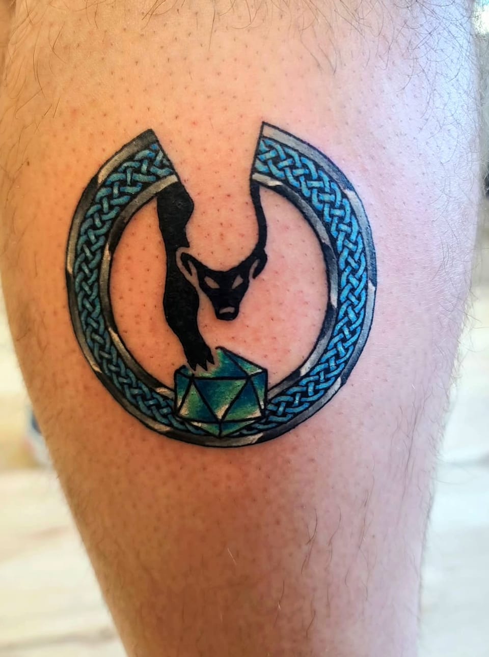 A horned animal head sits inside a blue Celtic ring tattoo.