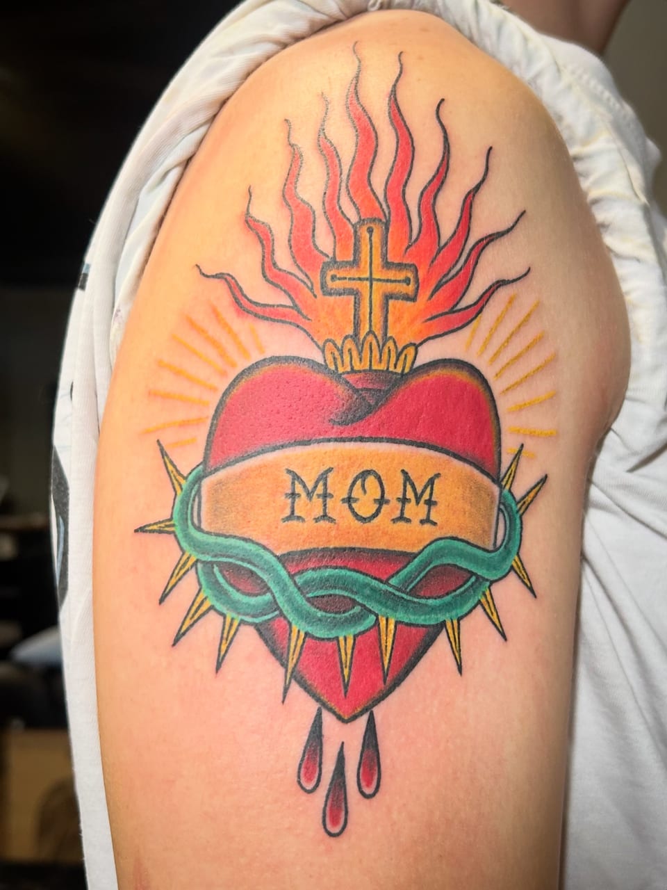 A red sacred-heart tattoo has a green thorn crown, a cross and a gold banner.