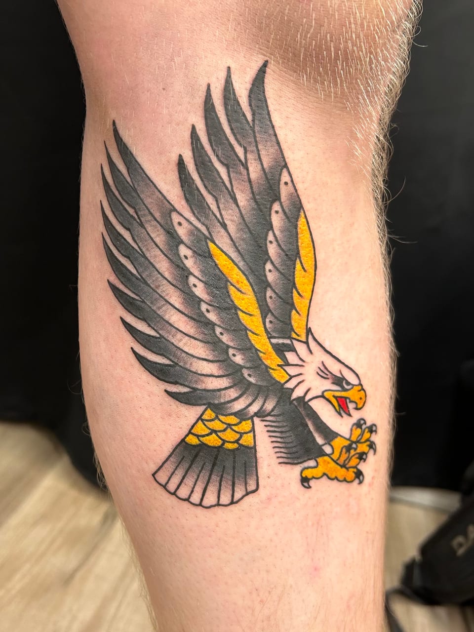 A black and yellow eagle tattoo spreads its wings along a forearm.