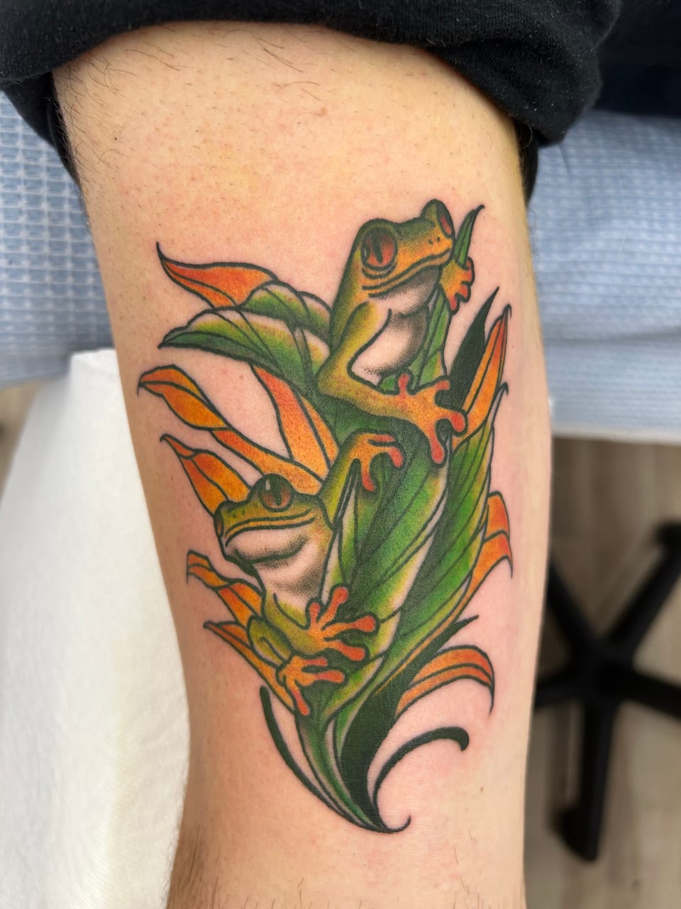 Green frogs climb orange and green leaves in a traditional tattoo.