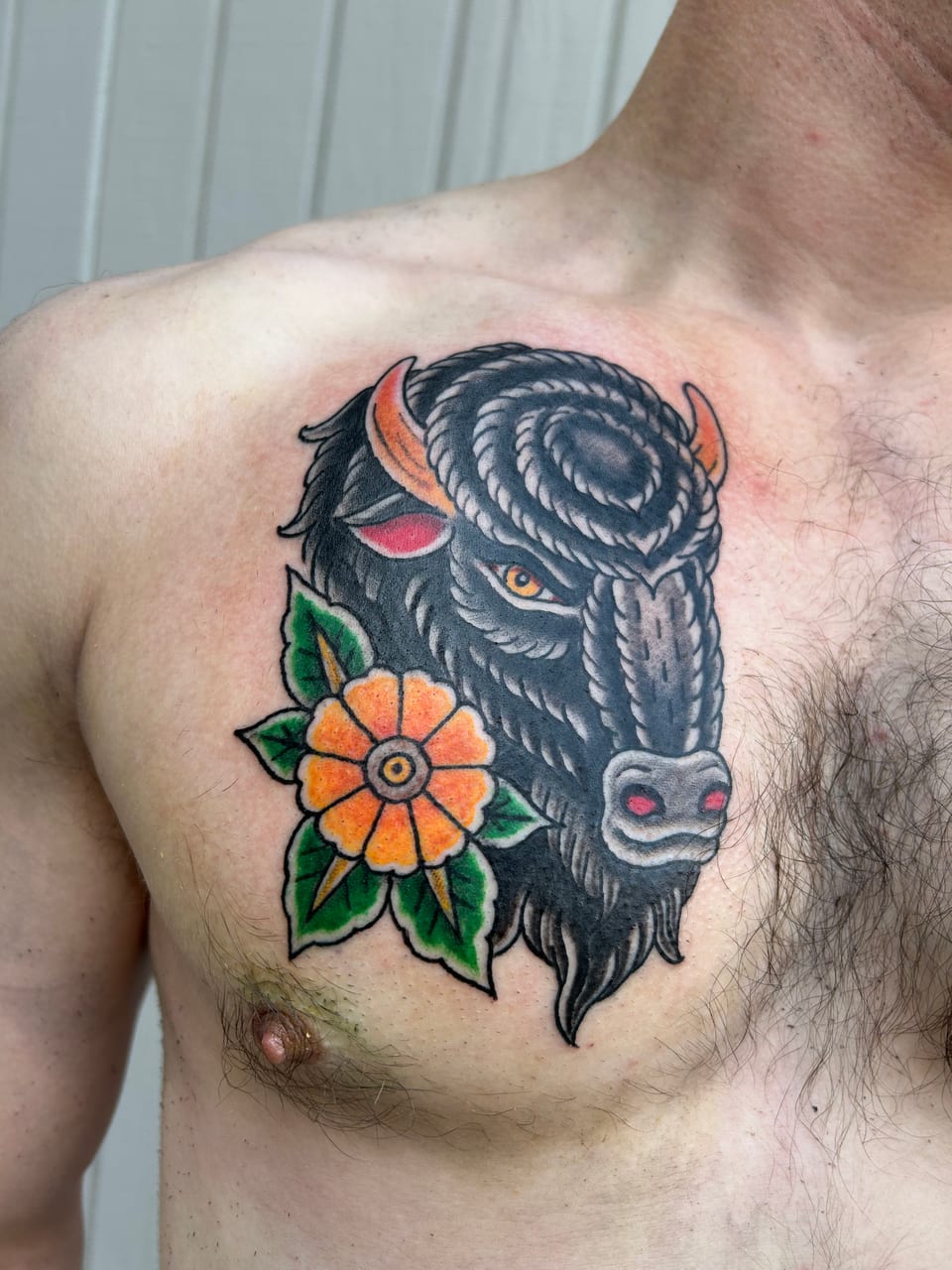 A black bison head tattoo sits beside an orange flower on the upper chest.