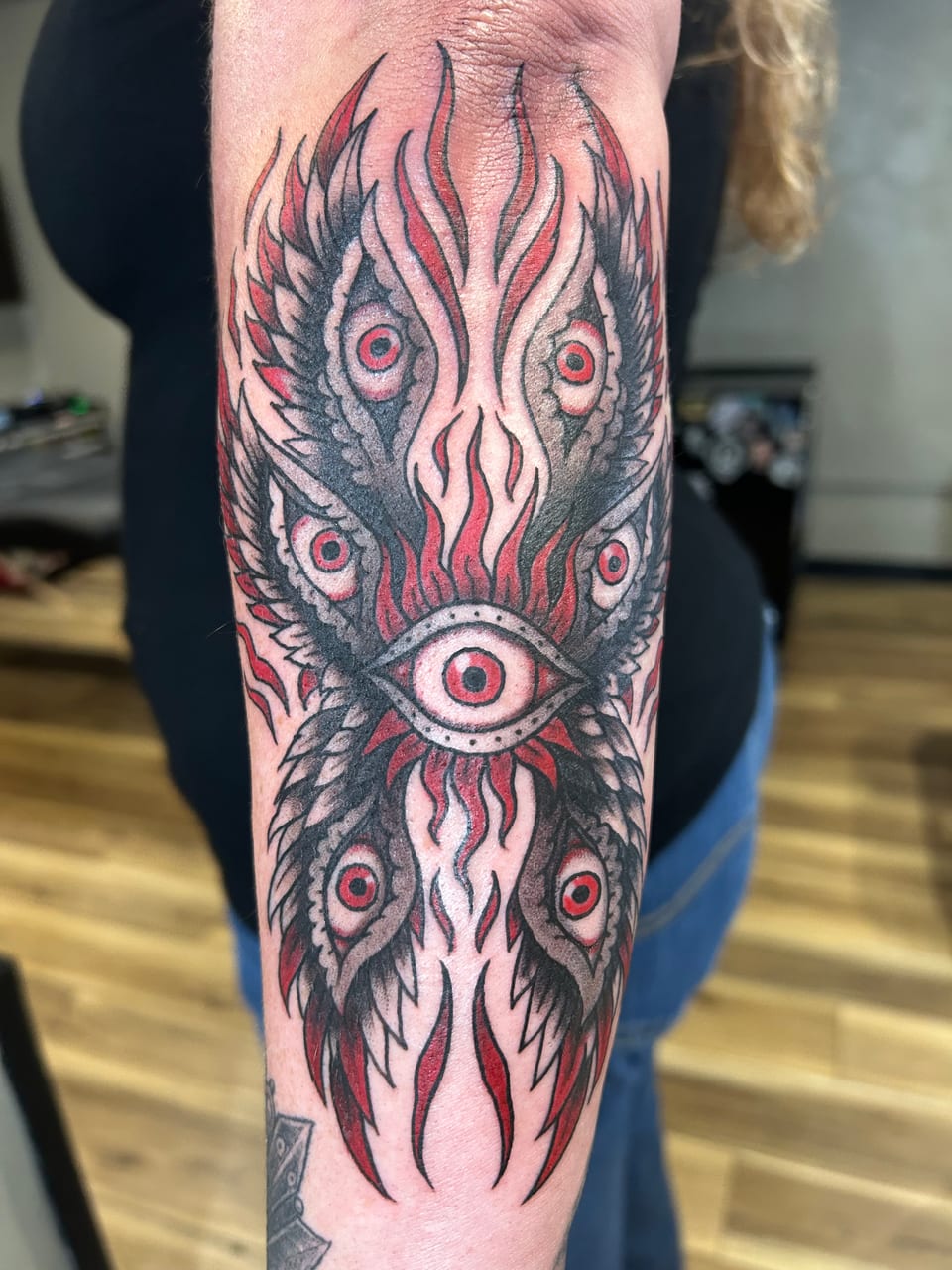 Red and black eyes with winged shapes fill a flame-like forearm tattoo.