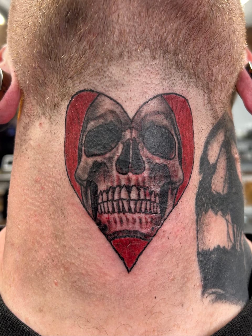 A skull framed by a red heart tattoo sits on the back of the neck.