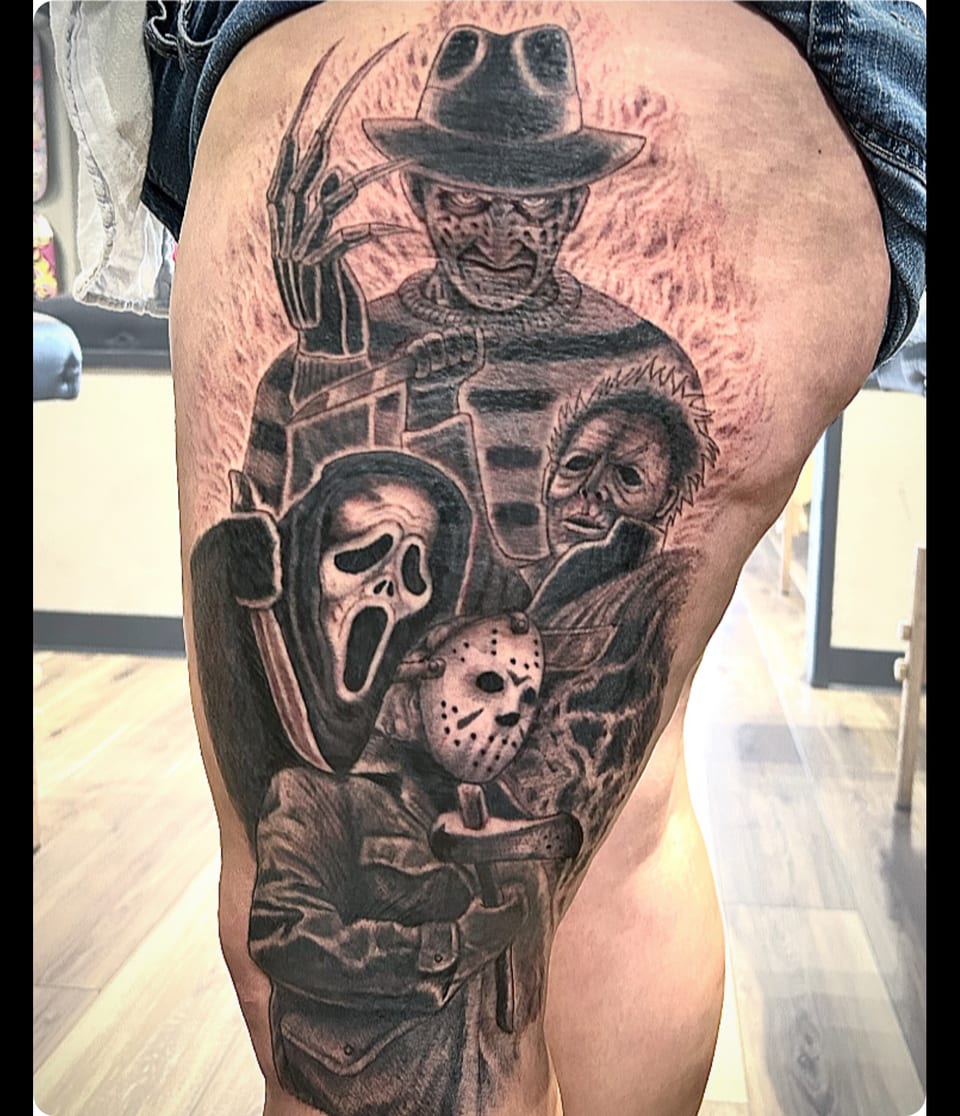 A black and grey tattoo brings masked horror figures together along a leg.