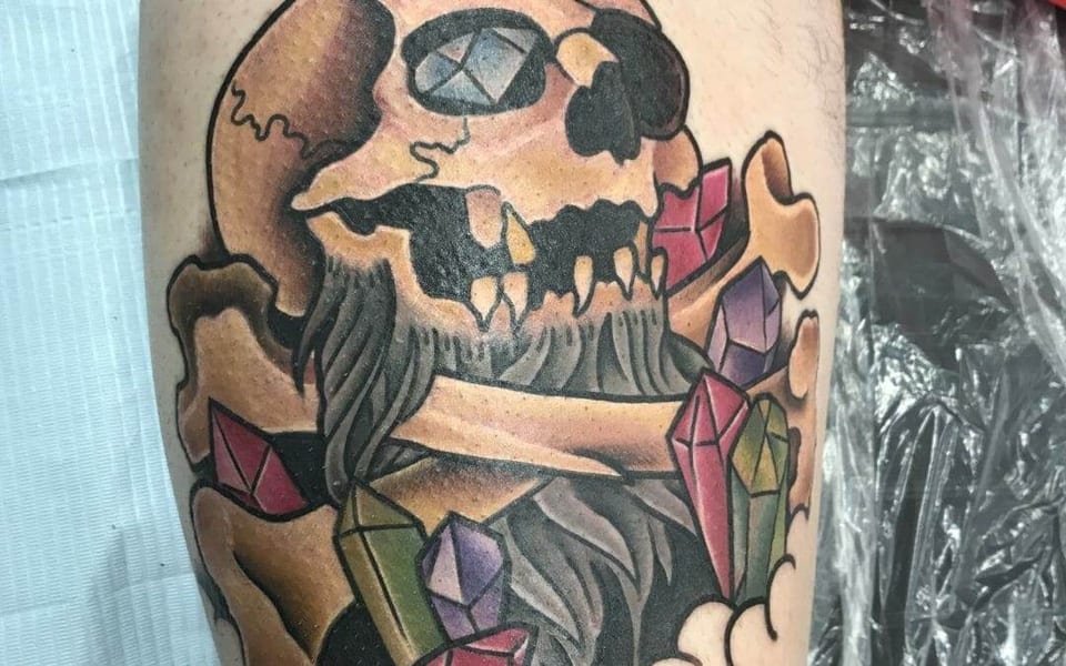 A traditional pirate skull with crossbones and colorful crystals covers an arm.