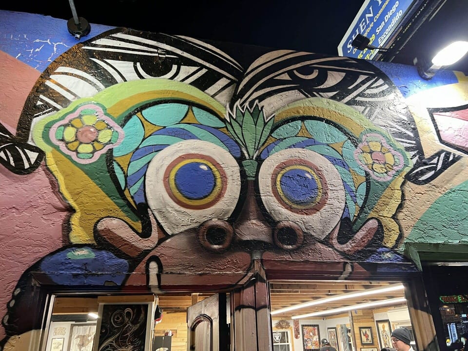 A brightly colored clown mural frames the open Funhouse Tattoo entrance at night.