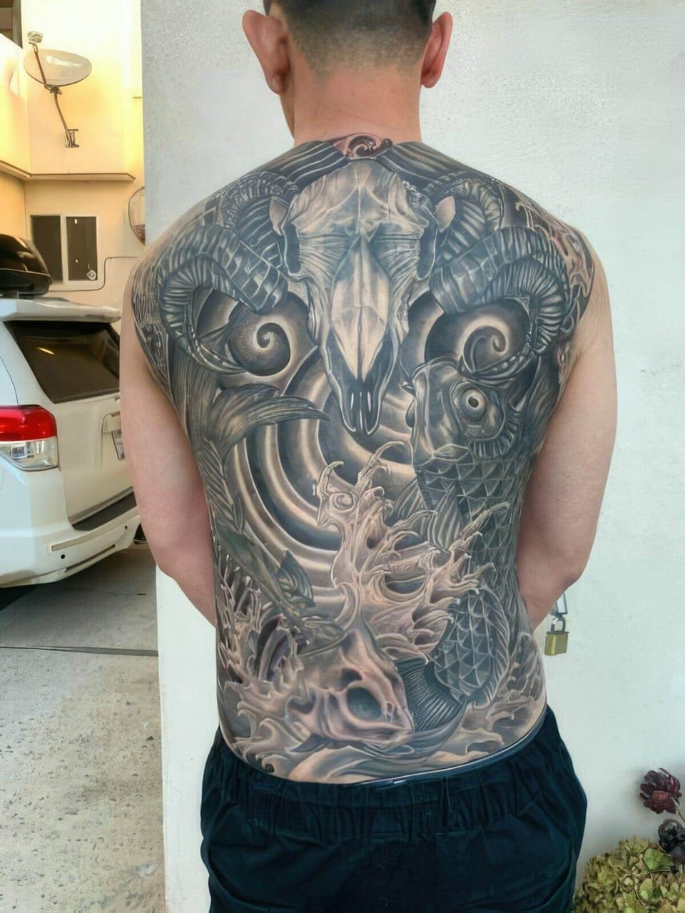 A black-and-grey biomechanical tattoo with horned skulls and curling forms spans the back.