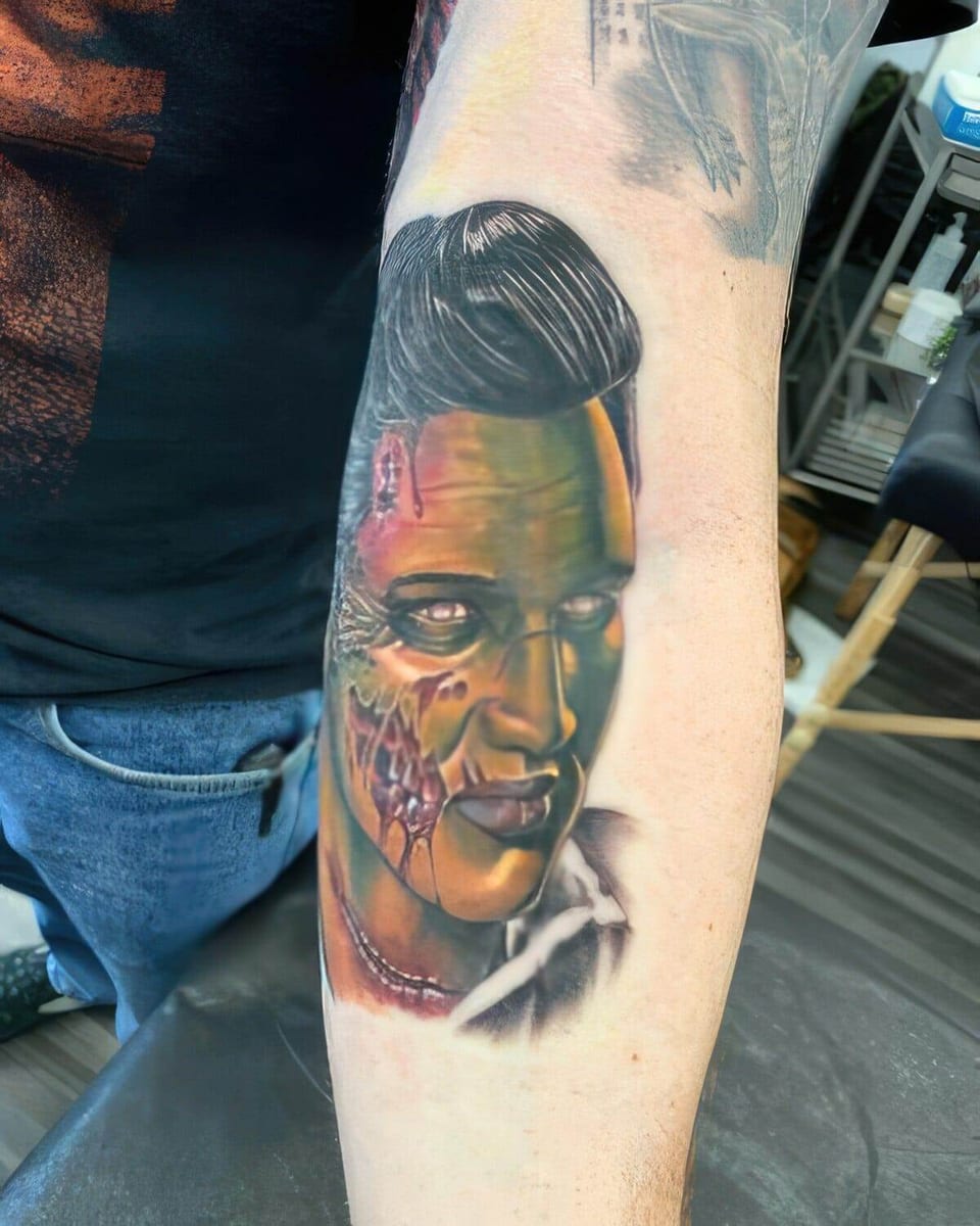 A colorful realistic portrait with slicked-back hair and a partly skeletal face covers a forearm.