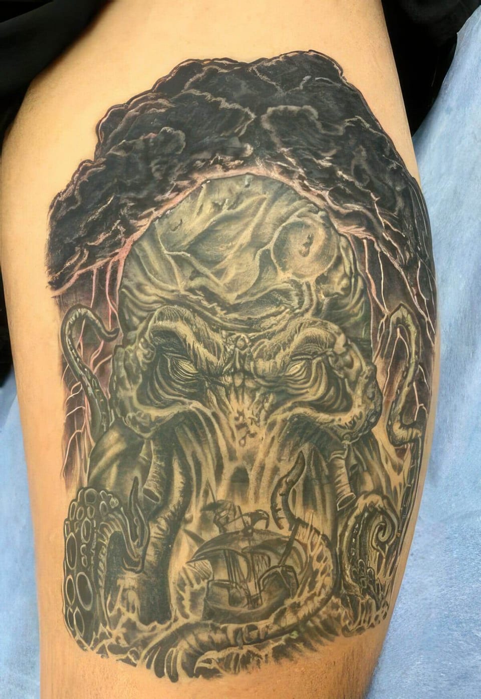 A green and black illustrative sea monster with tentacles and a sailing ship covers an upper arm.