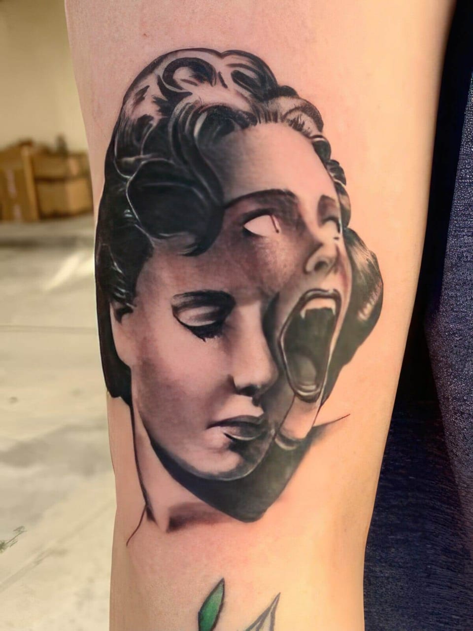 A black-and-grey realistic woman's face splits into calm and screaming expressions on an upper arm.