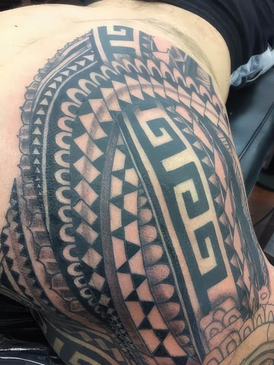 Black and grey Polynesian-style tribal tattoo with a Greek key panel covering an upper arm and side, tattooed by Seth Reynolds