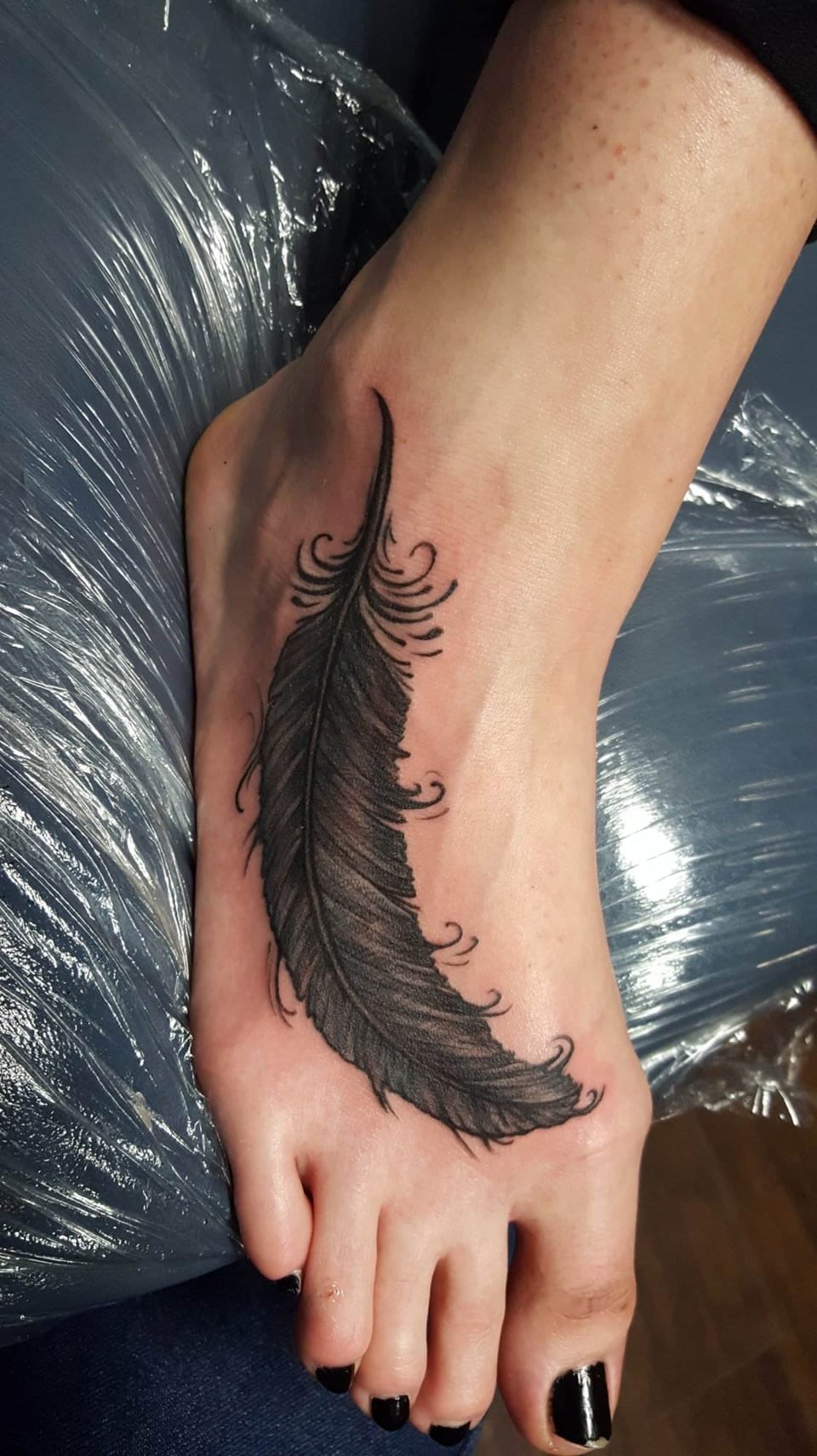 A black illustrative feather with curling tips stretches across the top of a foot.