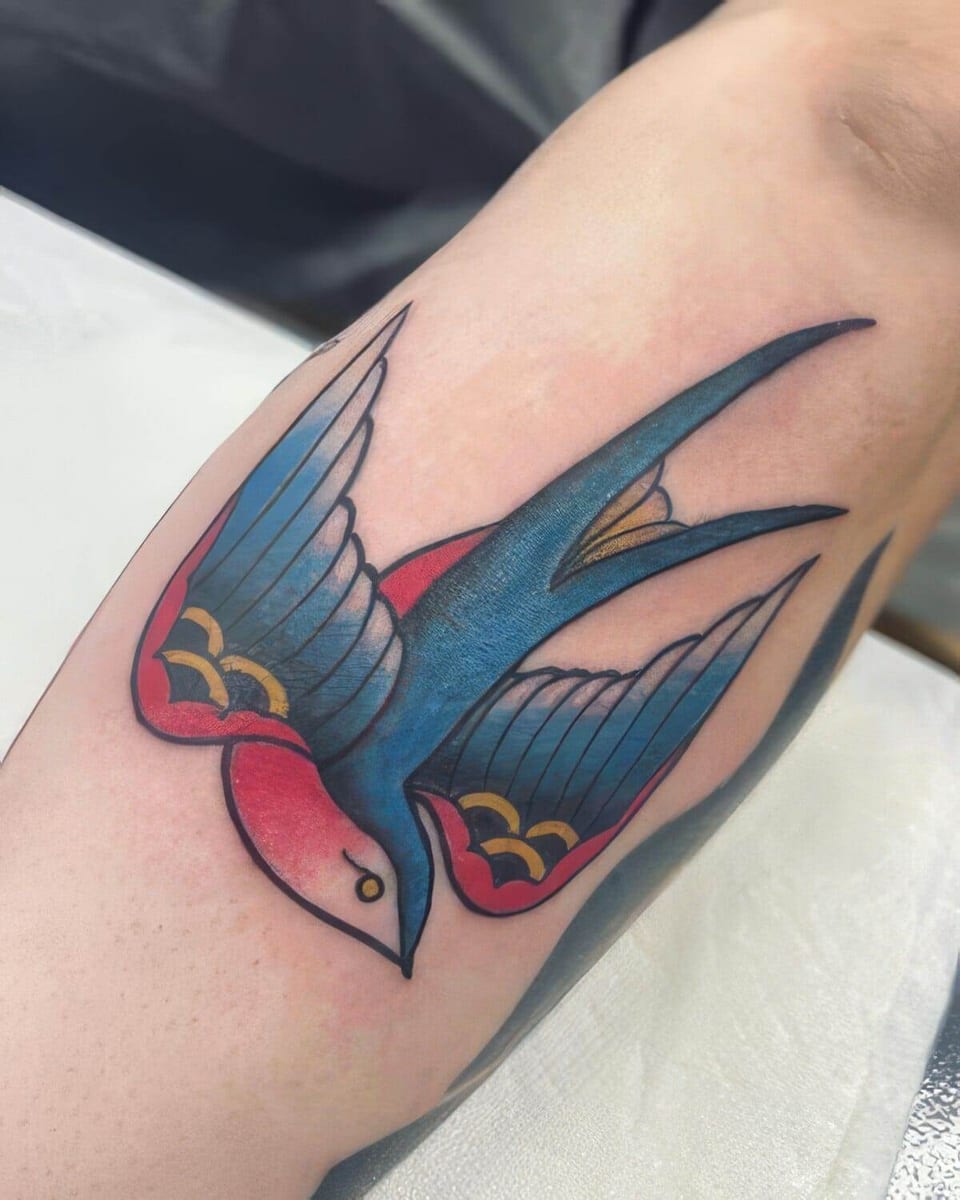 A traditional blue swallow with red and yellow wing accents covers a forearm.