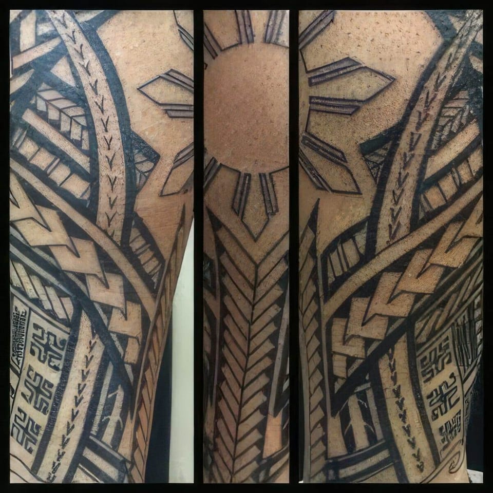 Black Polynesian-style tribal panels with a sun emblem tattooed on an arm, tattooed by Seth Reynolds