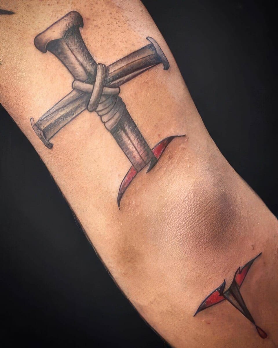 Black and grey illustrative crossed nails bound with cord sit above the elbow with red torn-skin accents.