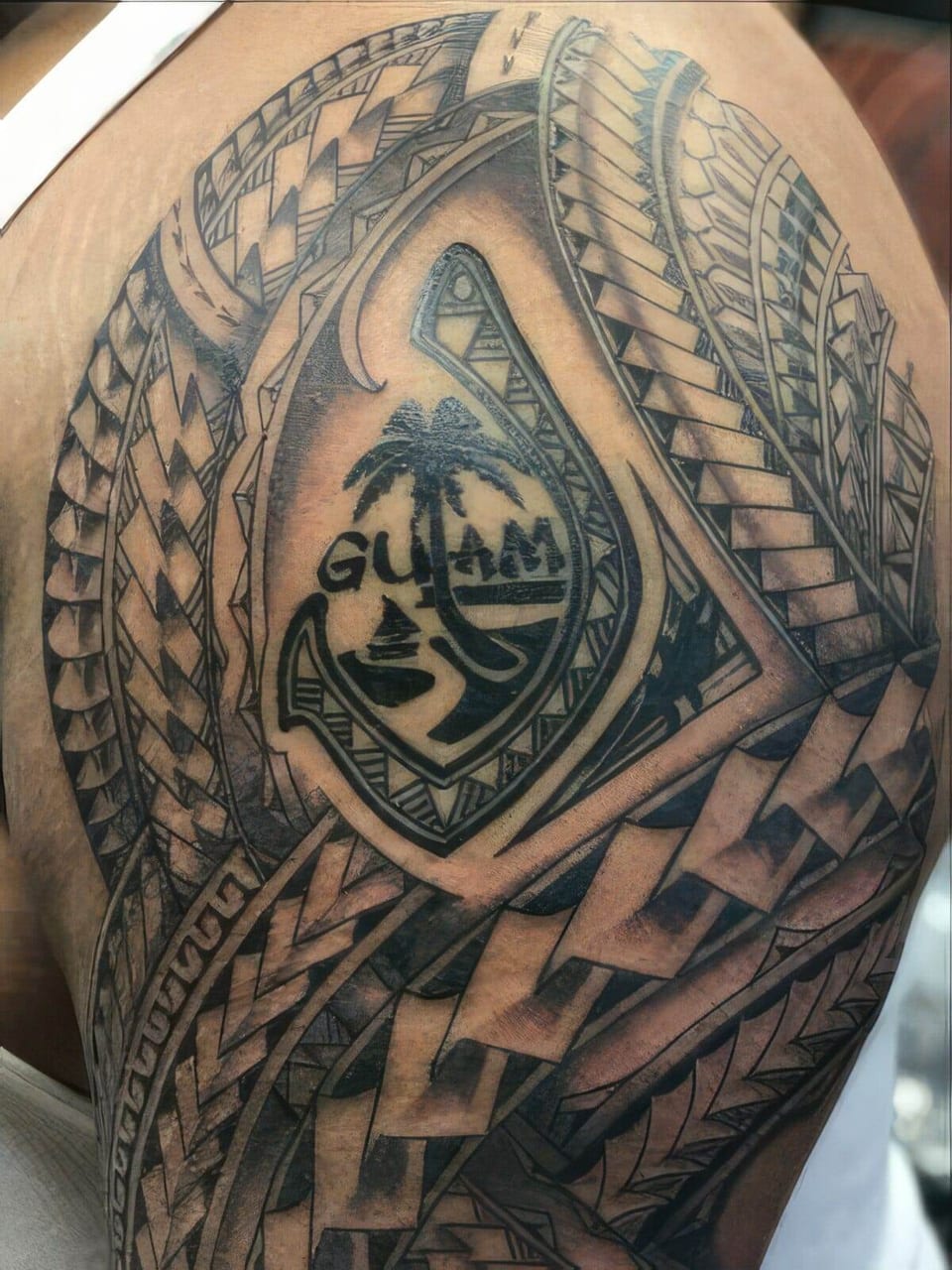 A black Polynesian tattoo with a Guam emblem and geometric panels covers a shoulder.
