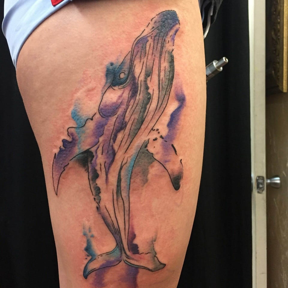 A watercolor-style whale with blue and purple splashes stretches along a thigh.