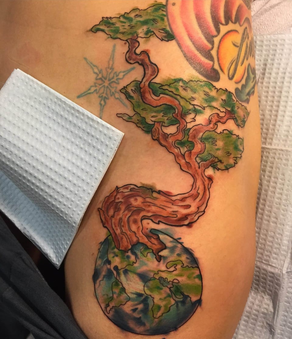 A colorful illustrative tree grows from a globe in a tattoo on the hip.
