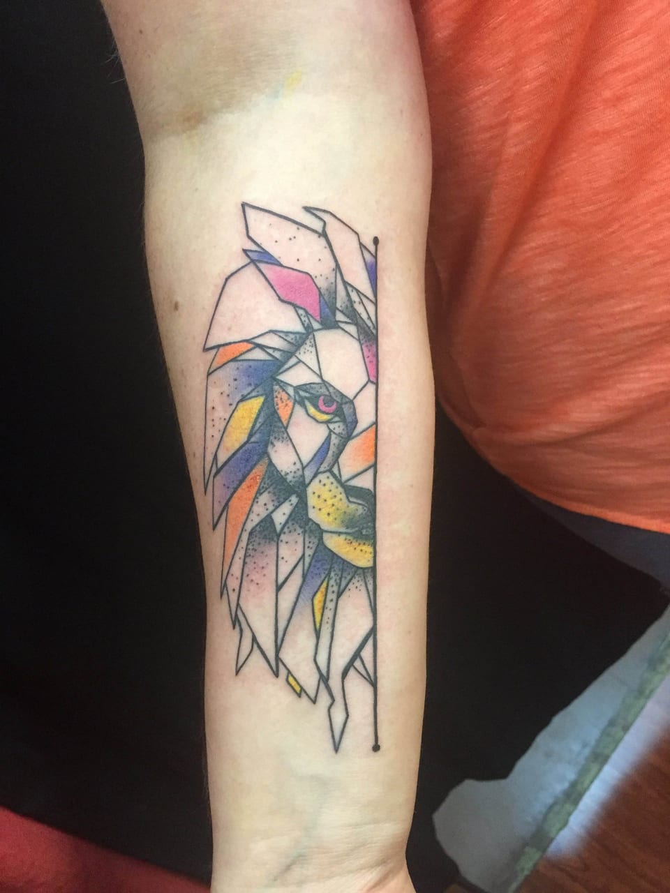 A colorful geometric half-lion face with angular facets and dotwork covers a forearm.