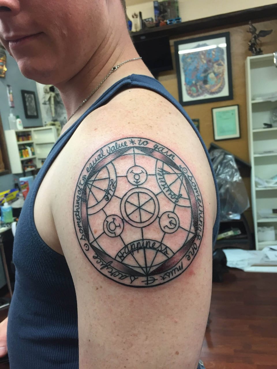 A black linework alchemy circle with symbols and script covers an upper arm.