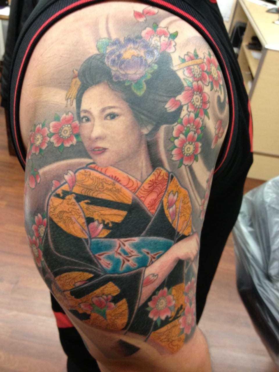 A colorful Japanese geisha in an orange kimono with cherry blossoms covers an upper arm.
