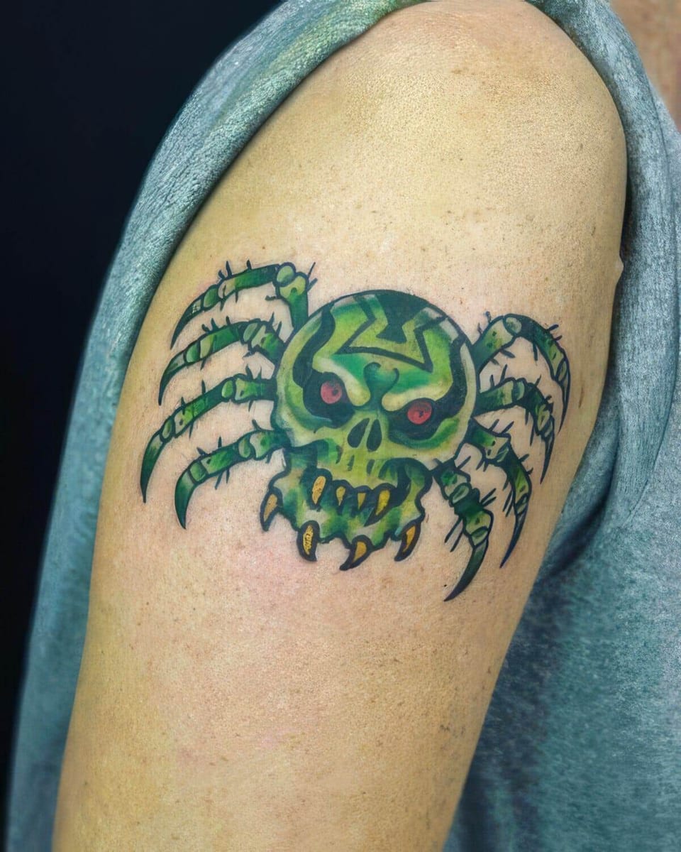 Traditional color spider with a green skull-shaped body and red eyes sits on the upper arm.