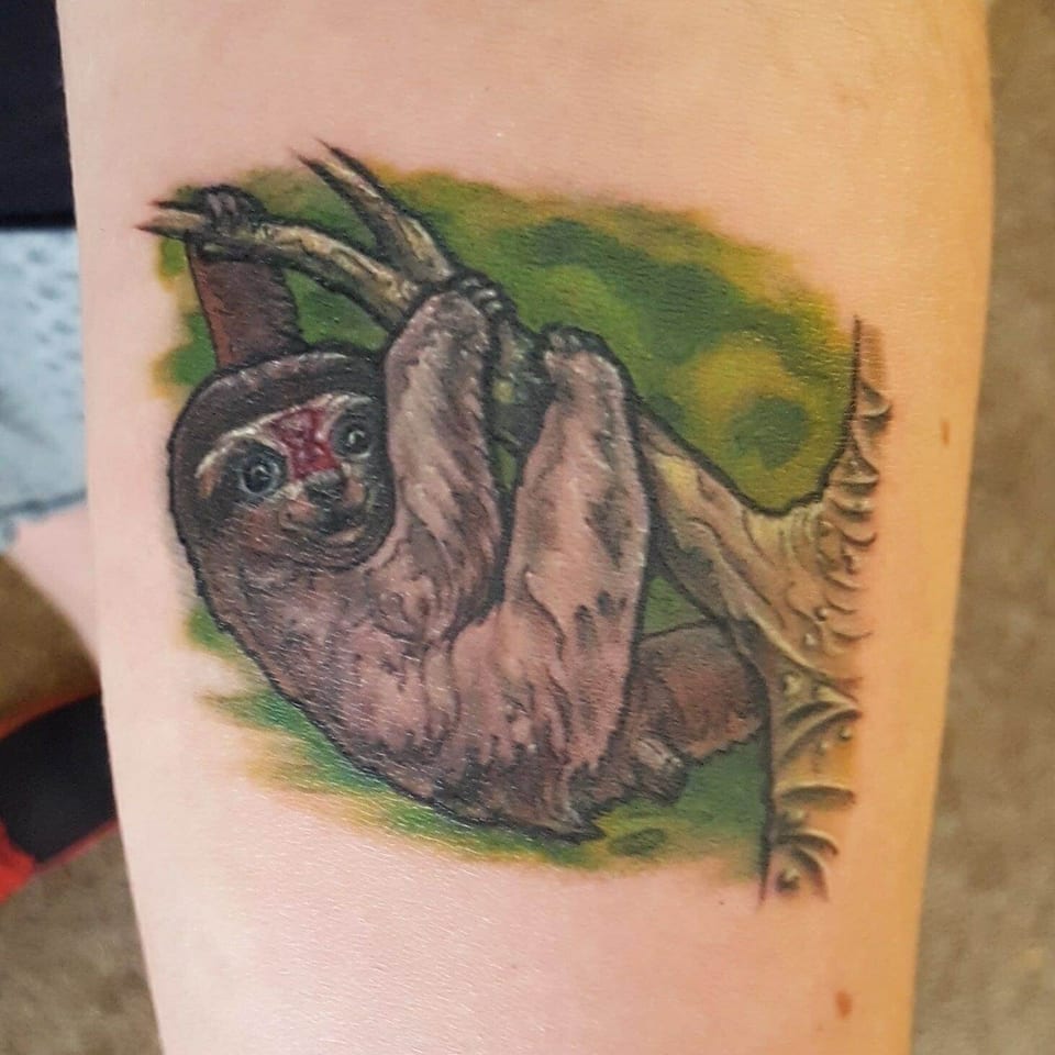 A colorful realistic sloth hanging from a branch sits on a thigh.