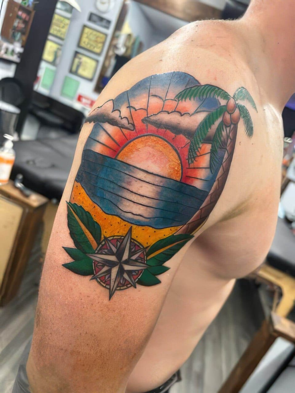 A colorful traditional sunset, palm tree and compass tattoo covers an upper arm.