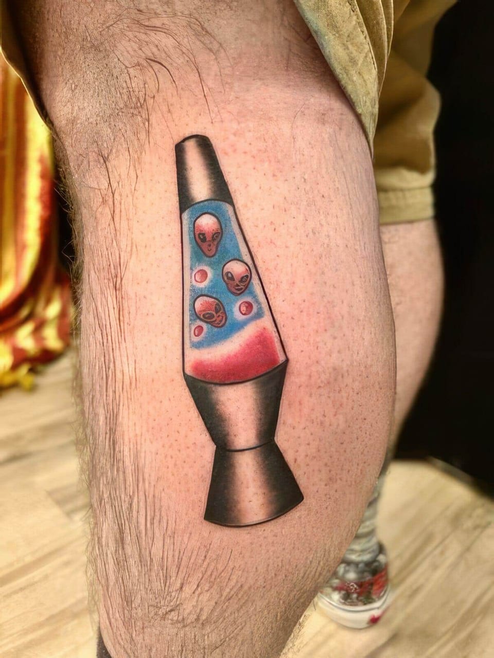 A colorful illustrative lava lamp filled with pink alien heads sits on a calf.