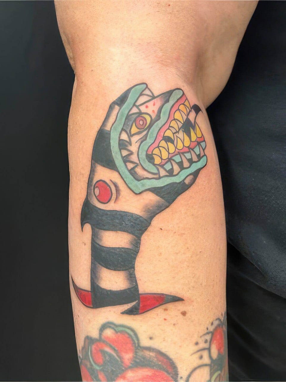 Traditional color snake head with teal jaws, yellow teeth and black bands sits on the forearm.