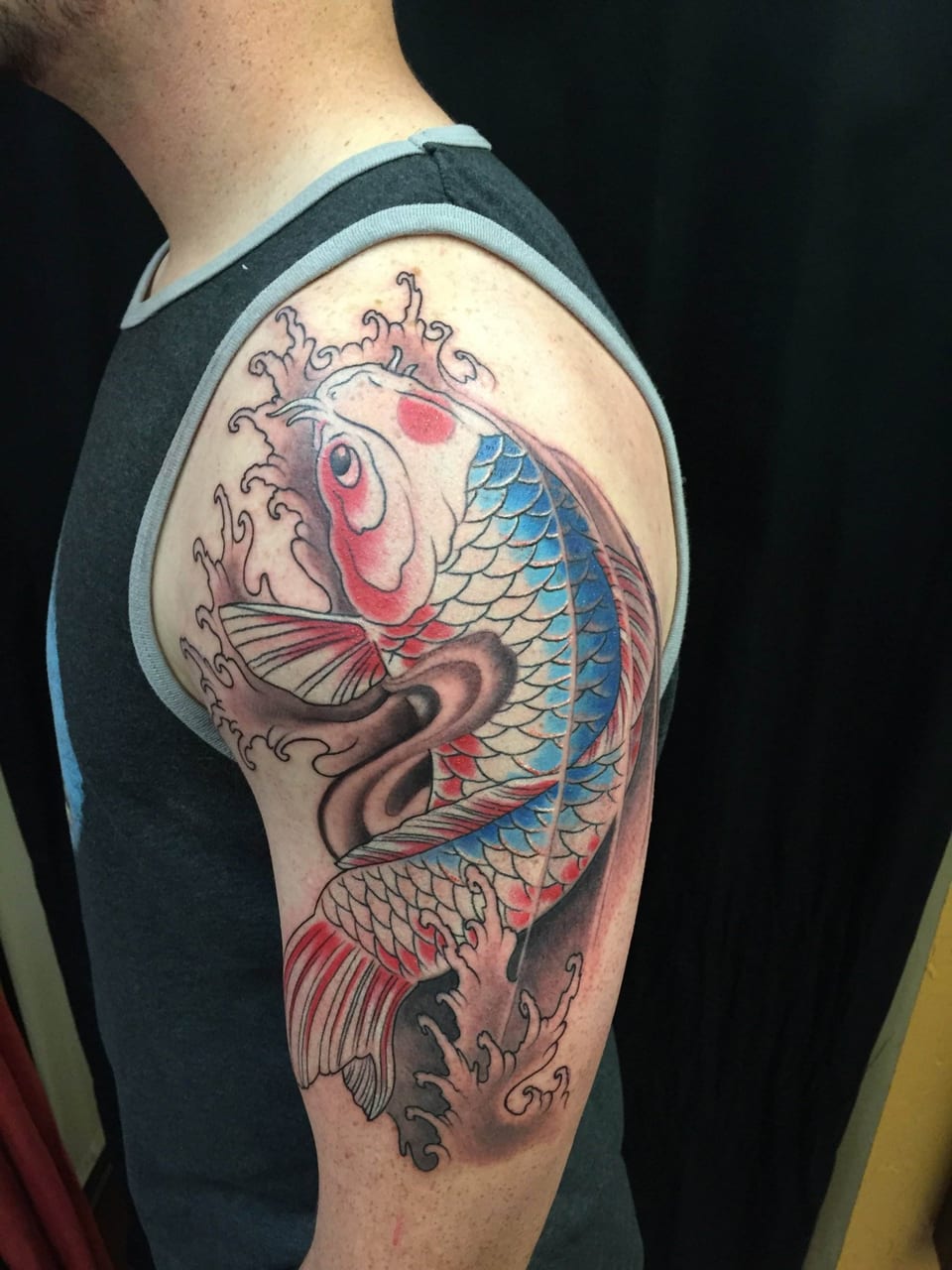 A Japanese koi tattoo with blue scales, red accents and grey waves covers an upper arm.