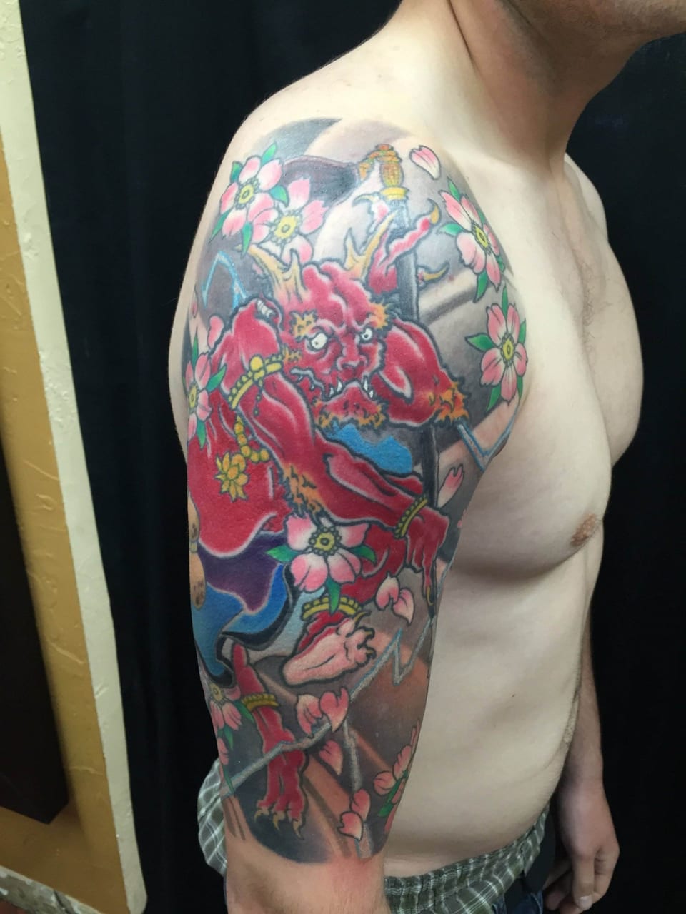 A colorful Japanese red demon holding a sword amid blossoms covers a shoulder and upper arm.