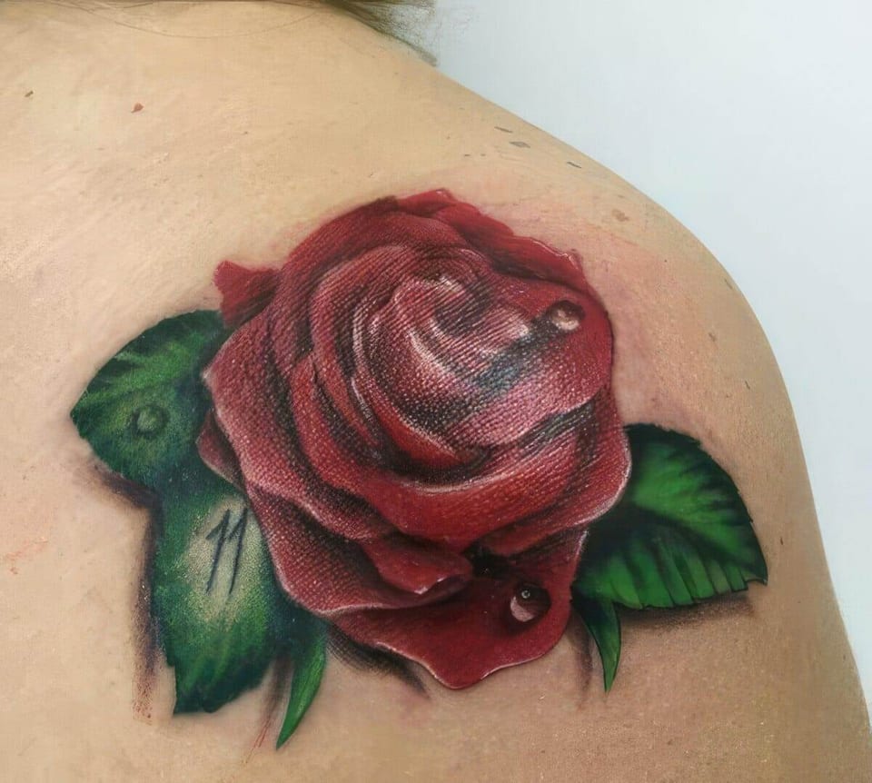 A realistic red rose with green leaves and water droplets covers a shoulder.