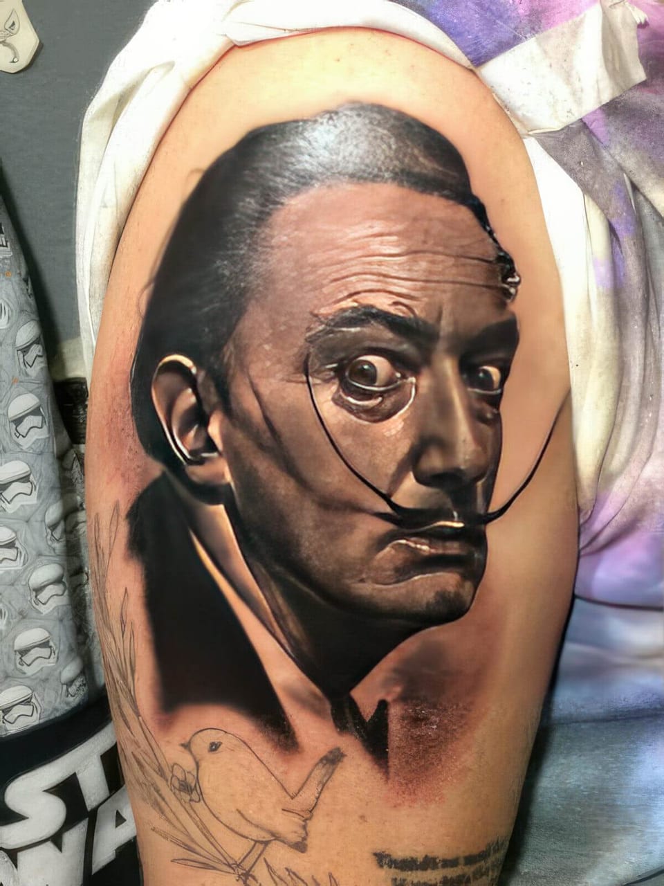 A black-and-grey realistic portrait of a man with a long upturned mustache covers an upper arm.