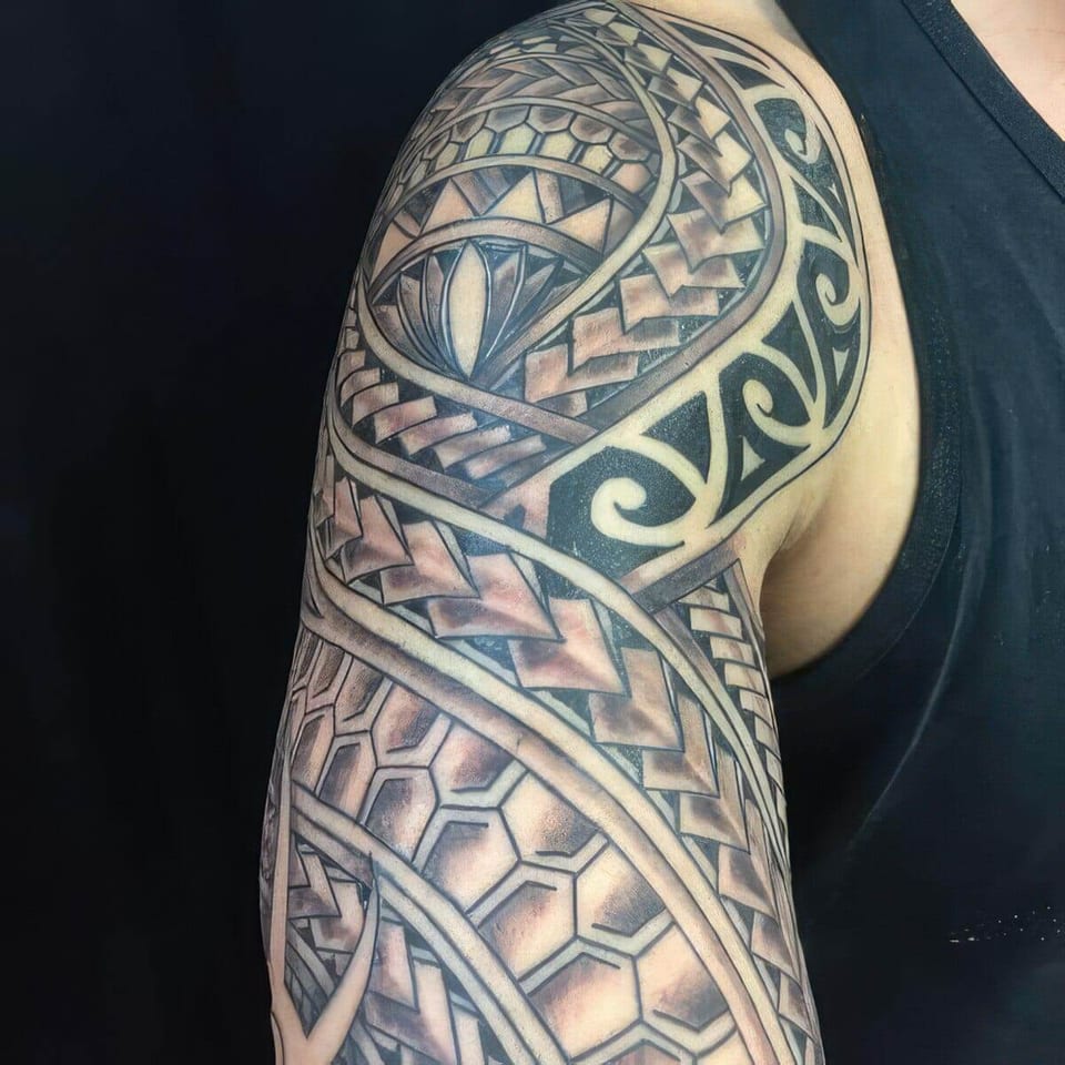 Black and grey Polynesian-style shoulder and arm piece with hexagon and wave patterns, tattooed by Seth Reynolds