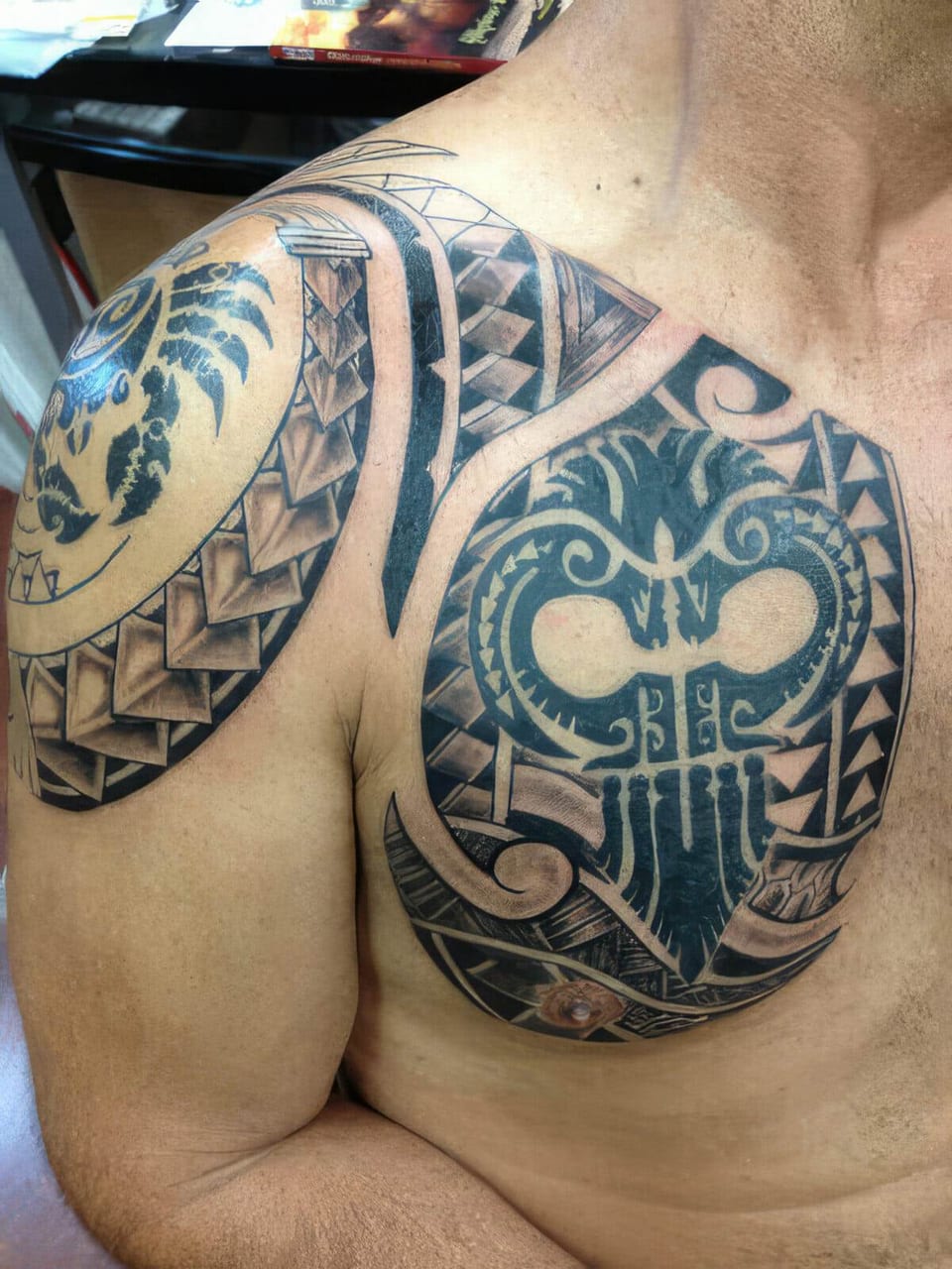 Black Polynesian-style mask and wing patterns tattooed on a chest and shoulder, tattooed by Seth Reynolds