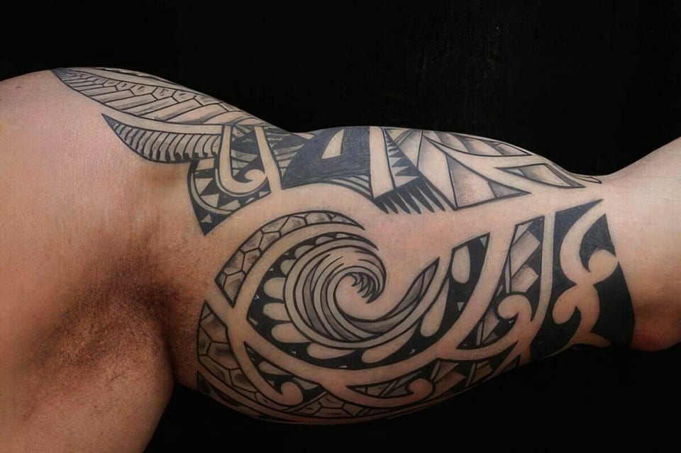 Black Polynesian-style spiral and wave pattern tattooed on an upper arm, tattooed by Seth Reynolds